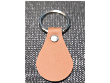 A simple brown leather keychain with a silver ring on a textured surface.