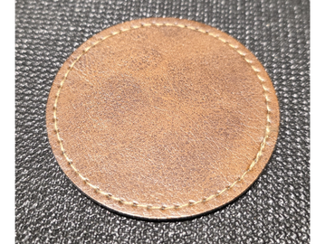 Close-up of a stitched brown leather patch on textured black fabric.