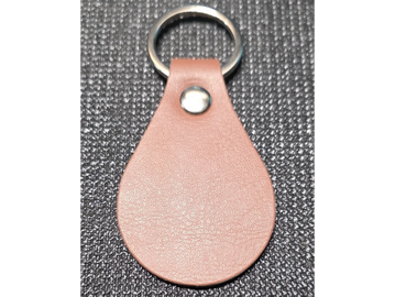 Brown leather keychain with a metal ring on a textured black surface.
